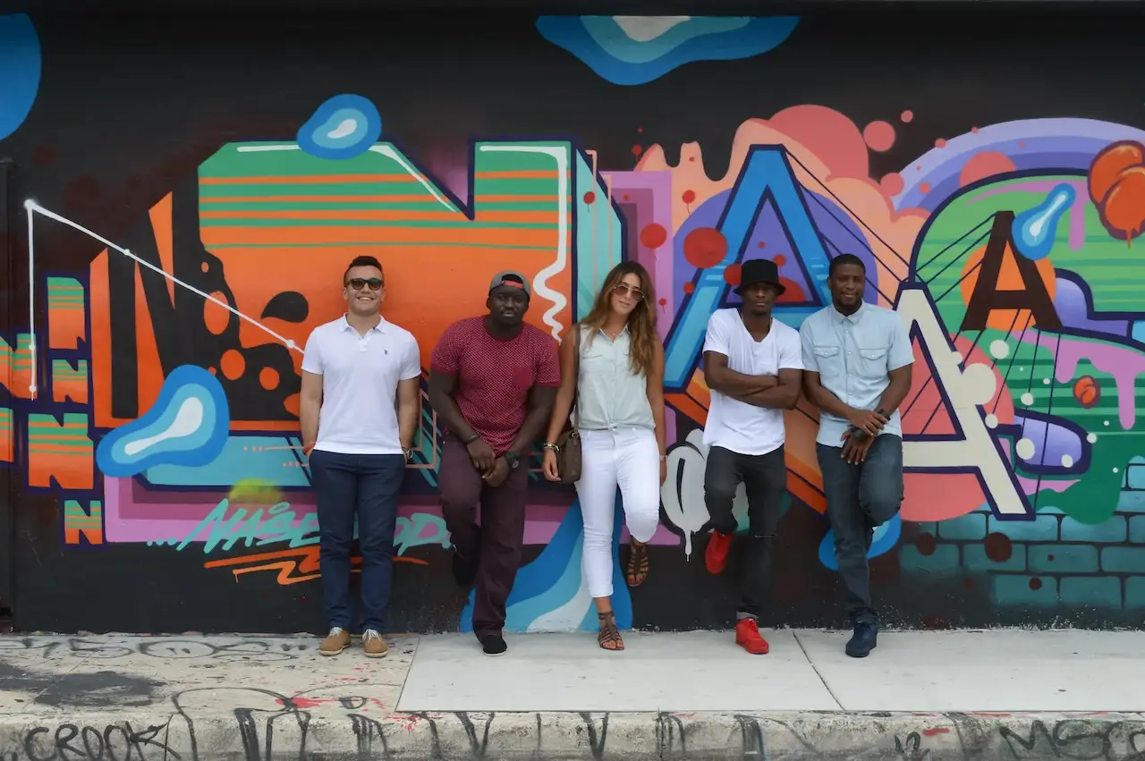 Group of friends posing in front of colorful street art mural in Miami.