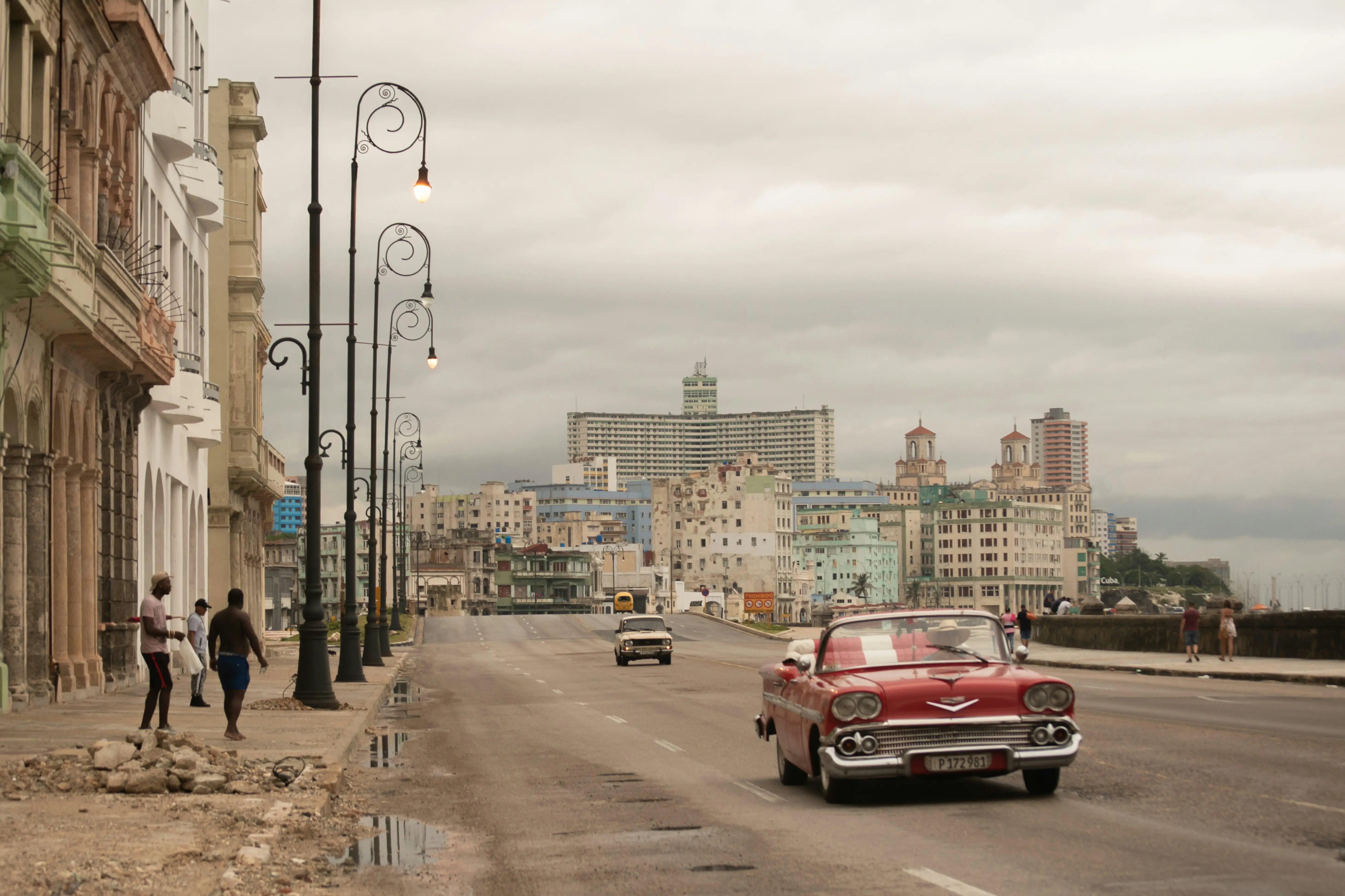 Red vintage American convertible driving along Havana’s Malecón waterfront with historic city skyline in the background.